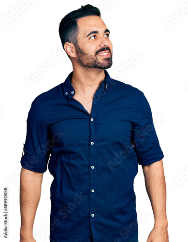 Young hispanic man with beard wearing casual blue shirt looking away to side with smile on face, natural expression. laughing confident.