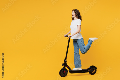 Side profile view young European woman she wear white blank t-shirt casual clothes driving electric scooter look camera isolated on plain yellow orange background studio portrait. Lifestyle concept.