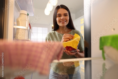 Happy woman taking away beeswax food wrap, view from refrigerator