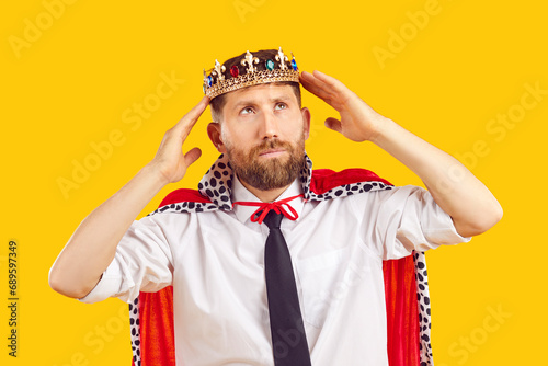 Ambitious self confident employee in king costume dreams of becoming business director. Bearded man in royal cloak and office shirt puts golden crown on head and looks away with dreamy face expression