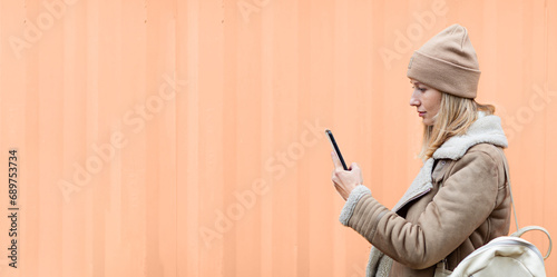 Trendy color of the year 2024 peach fuzz. Woman using mobile phone outdoor. Web banner mockup with copy space