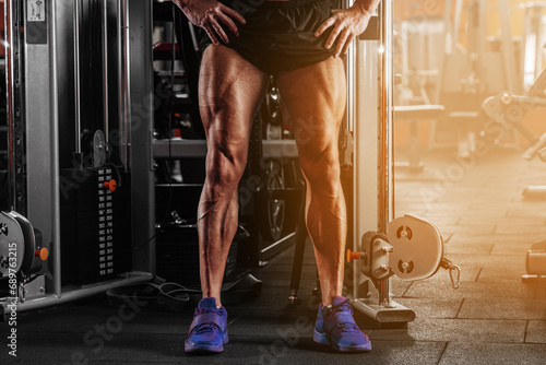 Closeup image of a strong man with muscular legs . posing at gym