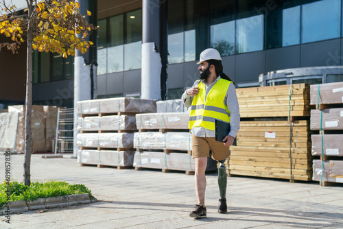 Caucasian male with beard and safety gear stands at construction, prosthetic leg visible.