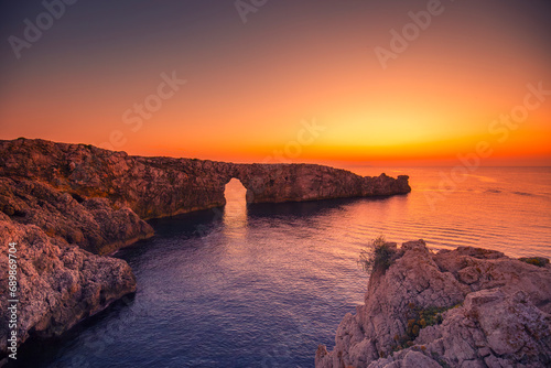 Krajobraz morski, pomarańczowy zachód słońca, skaliste wybrzeże wyspy Minorka (Menorca), Hiszpania 