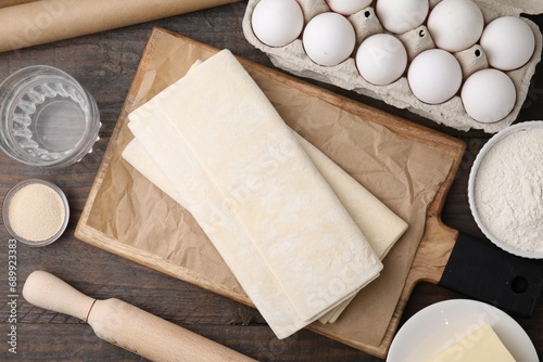 Raw puff pastry dough and ingredients on wooden table, flat lay