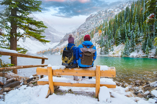 Lake Agnes by Lake Louise Banff National Park with snowy mountains in the Canadian Rocky Mountains during winter. A couple of men and women sitting on a bench by the emerald green lake in Canada with