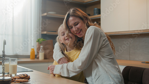 Mother and little daughter cuddle hold hands dancing sitting at table in kitchen breakfast loving mom dance with child girl hugging embracing kid enjoy tender family bonding cuddling. Happy motherhood