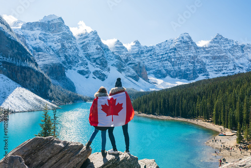 Tourists draped in Canadian flag looking beautiful scenery of Moraine lake. Banff National Park. Canadian Rockies. Alberta, Canada.