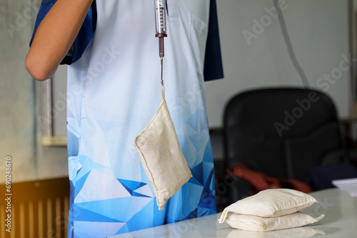 Asian students perform a physics experiment using a Spring Balance, a cylinder connected to a sandbag, and pulled up to measure the weight of the sandbag. Soft and selective focus. 