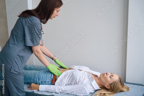 Family doctor performing abdominal exam of mature woman
