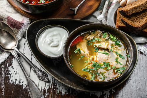 Chicken soup with meat, greens and sour cream on bowl on rustic wooden background. Healthy food, top view
