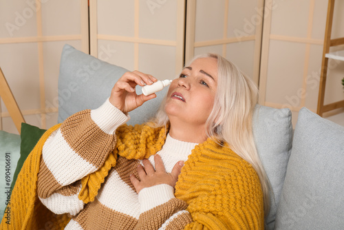 Sick mature woman with nasal drops at home