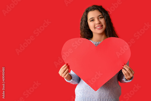 Happy young woman with paper heart on red background