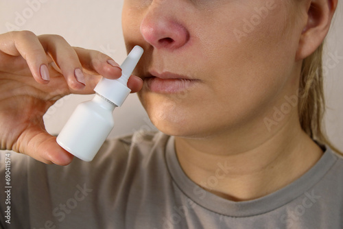 Close up of sick woman with red nose using a nose spray, blurry background