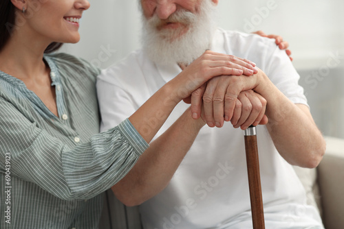 Senior man with walking cane and young woman indoors, closeup
