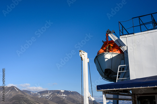 Safety measures on a large ship, lifeboat hanging from the top side of the ship, sunny summer day cruising in the arctic 