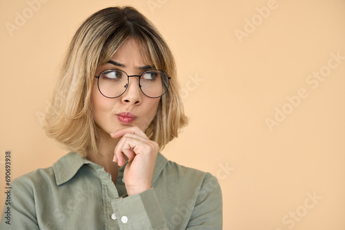 Cute curious blonde get z girl holding hand on chin looking interested aside isolated on beige background. Young woman thinking of shopping offers, choosing or feeling doubts, making decision.