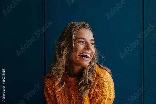 Happy young blond hair woman in yellow sweater looking away while standing on blue background