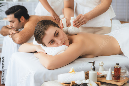 Hot herbal ball spa massage body treatment, masseur gently compresses herb bag on couple customer body. Tranquil and serenity of aromatherapy recreation in day lighting ambient at spa salon. Quiescent