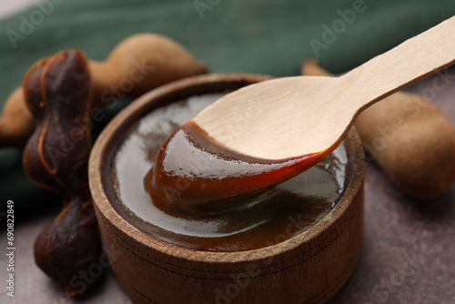 Taking tasty tamarind sauce with spoon from bowl on brown table, closeup