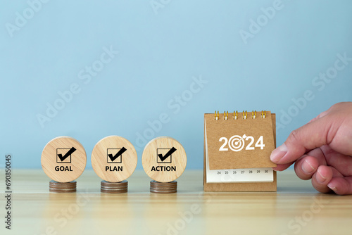 Happy New Year 2024 banner background. 2024 numbers year with target dart icon on desk calendar with hand turns over a calendar sheet. Goal, Plan, Action on wooden cube. Business goals plan action.