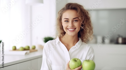 Young attractive joyful woman with green apple smile on kitchen background. Nutritionist, vegetarianism, healthy eating. The benefits of fruit for breakfast.