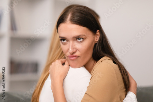 Dishonest young woman hugging her crying girlfriend at home