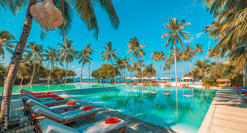 Relax tourism landscape. Luxurious beach resort with swimming pool and beach chairs or loungers leisure lifestyle, under umbrellas, palm trees, blue sky. Summer travel and vacation background concept 