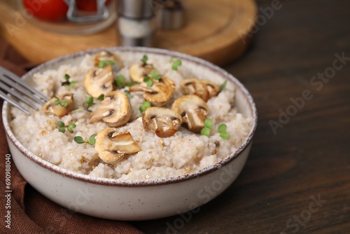 Delicious barley porridge with mushrooms and microgreens in bowl on wooden table, closeup
