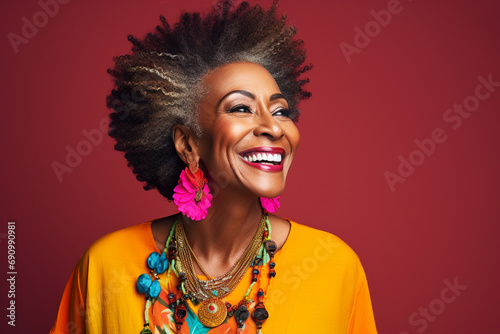 Mature mid aged dark skin woman with afro hair isolated in flat red background, happily smiling black woman wearing fancy jewelries and colorful cloths close up portrait, healthy skin care cosmetics