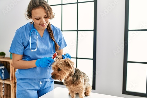 Young beautiful hispanic woman veterinarian examining dog with otoscope at home