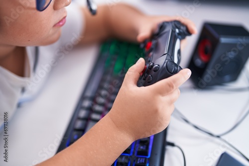 Adorable hispanic boy streamer playing video game using joystick at gaming room