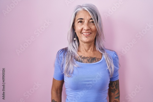 Middle age woman with tattoos standing over pink background with a happy and cool smile on face. lucky person.