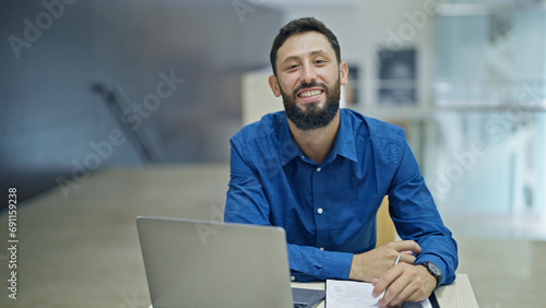 Young hispanic man business worker using laptop taking notes at the office