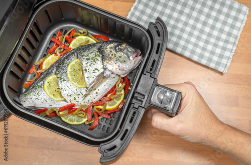 HAND COOKING A GILTHEAD SEA BREAM WHOLE FISH RECIPE IN AIR FRYER IN THE KITCHEN. TOP VIEW.