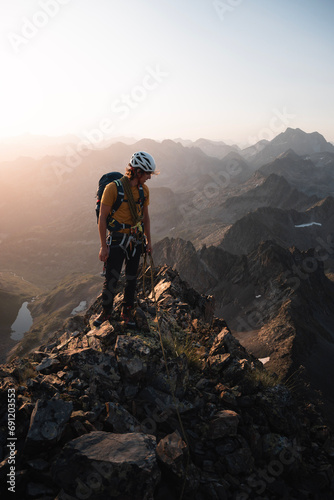 Young mountaineer enjoys the landscape of the Pyrenees mountains during a beautiful and warm summer sunrise while climbing an alpine rock ridge