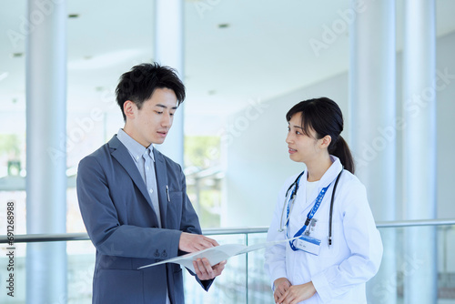病院内にてスーツを着たMRの男性と話をする女性医師