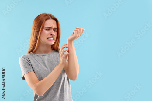 Suffering from allergy. Young woman scratching her arm on light blue background, space for text