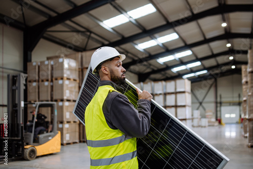 Handsome worker carrying solar panel in warehouse, factory. Solar panel manufacturer, solar manufacturing.