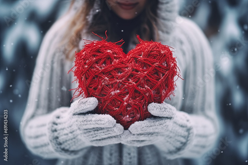 mujer joven sosteniendo un corazón de lana rojo entre sus manos, vistiendo ropa de invierno, sobre fondo de bosque nevando , concepto San Valentín 