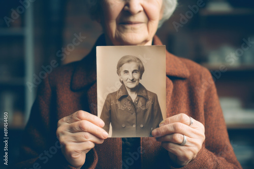 Senior Woman Holding a Vintage Photo of Her Younger Self - Memories and the Passage of Time in a Single Image