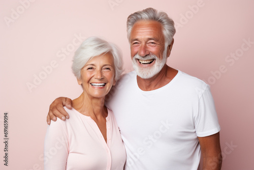 Stock photography portrait of an old couple smiling candidly, wearing a plain white t-shirt, isolated on a plain light pink colored background