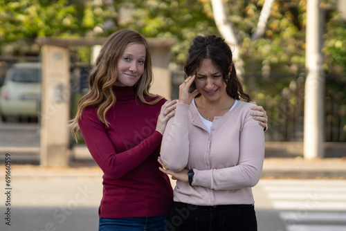 Happy false friend consoling a desperate woman in the street