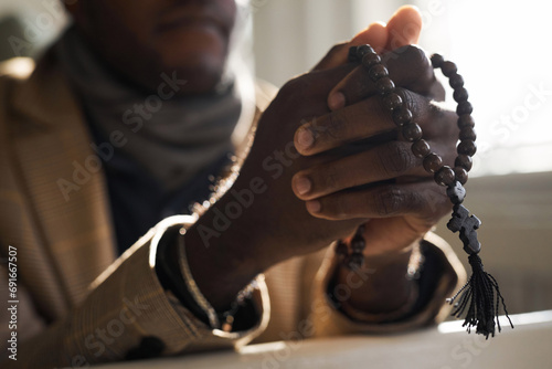 Close up of unrecognizable Black man praying in church with focus on hands holding rosary beads, copy space