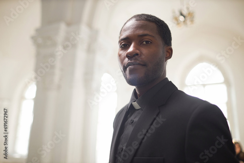 Portrait of young Black man as religious priest looking at camera in ethereal church setting, copy space