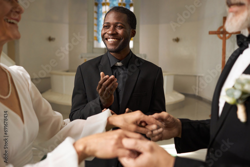 Waist up portrait of smiling Black man as priest officiating wedding in church, copy space