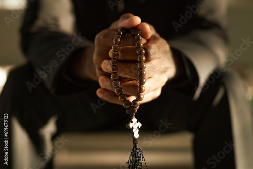 Closeup of priest holding wooden rosary beads and praying in ethereal sunlight, copy space