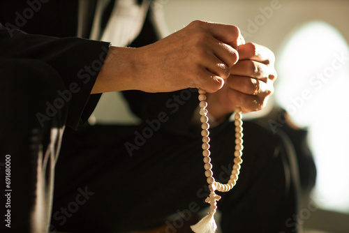 Side view closeup of unrecognizable man holding rosary beads in prayer lit by sunlight, copy space