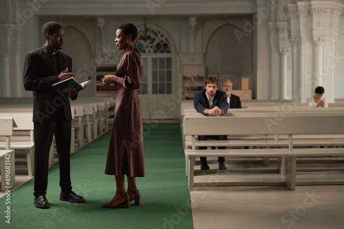 Side view portrait of African American pastor advising woman after Sunday service in catholic church, copy space