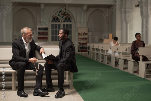 Full length portrait of African American pastor advising senior man after Sunday service in catholic church, copy space